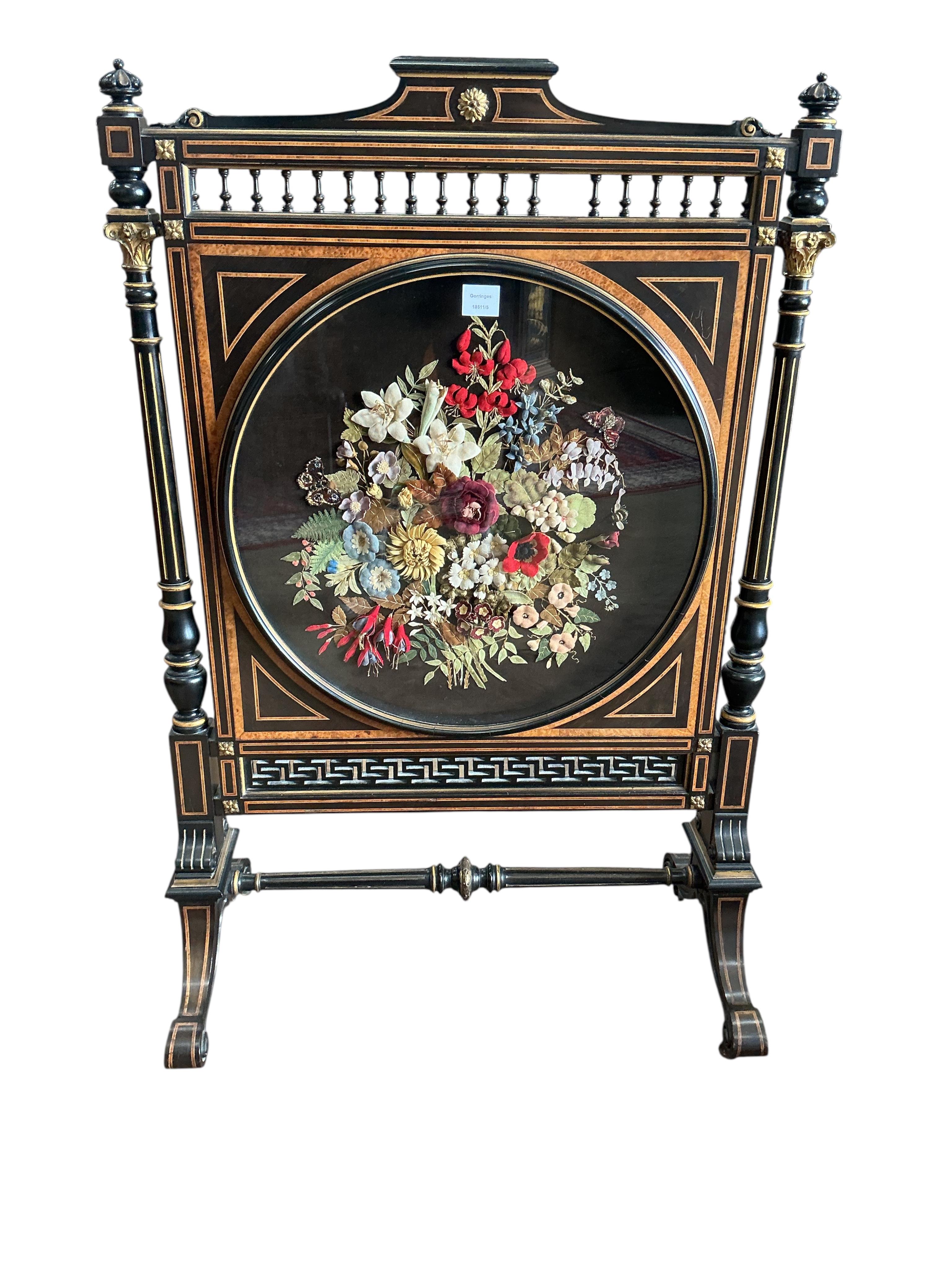 A late Victorian gilt metal mounted part ebonised bird's eye maple firescreen inset circular woolwork floral banner, width 79cm, height 122cm
